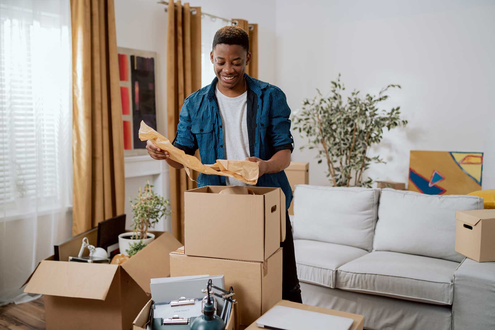 Unpacking cardboard boxes after moving, man cleans new apartment cluttered with things from previous home, looks at items, planning decorations, living room furnishings